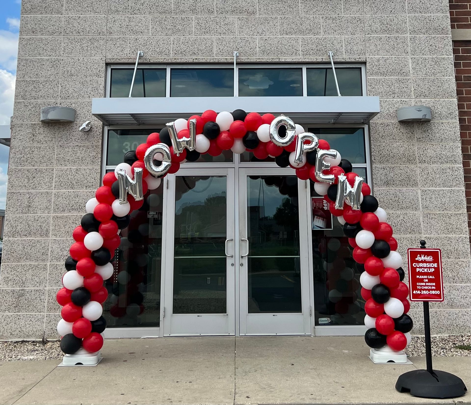 A red white and black balloon arch that says now open