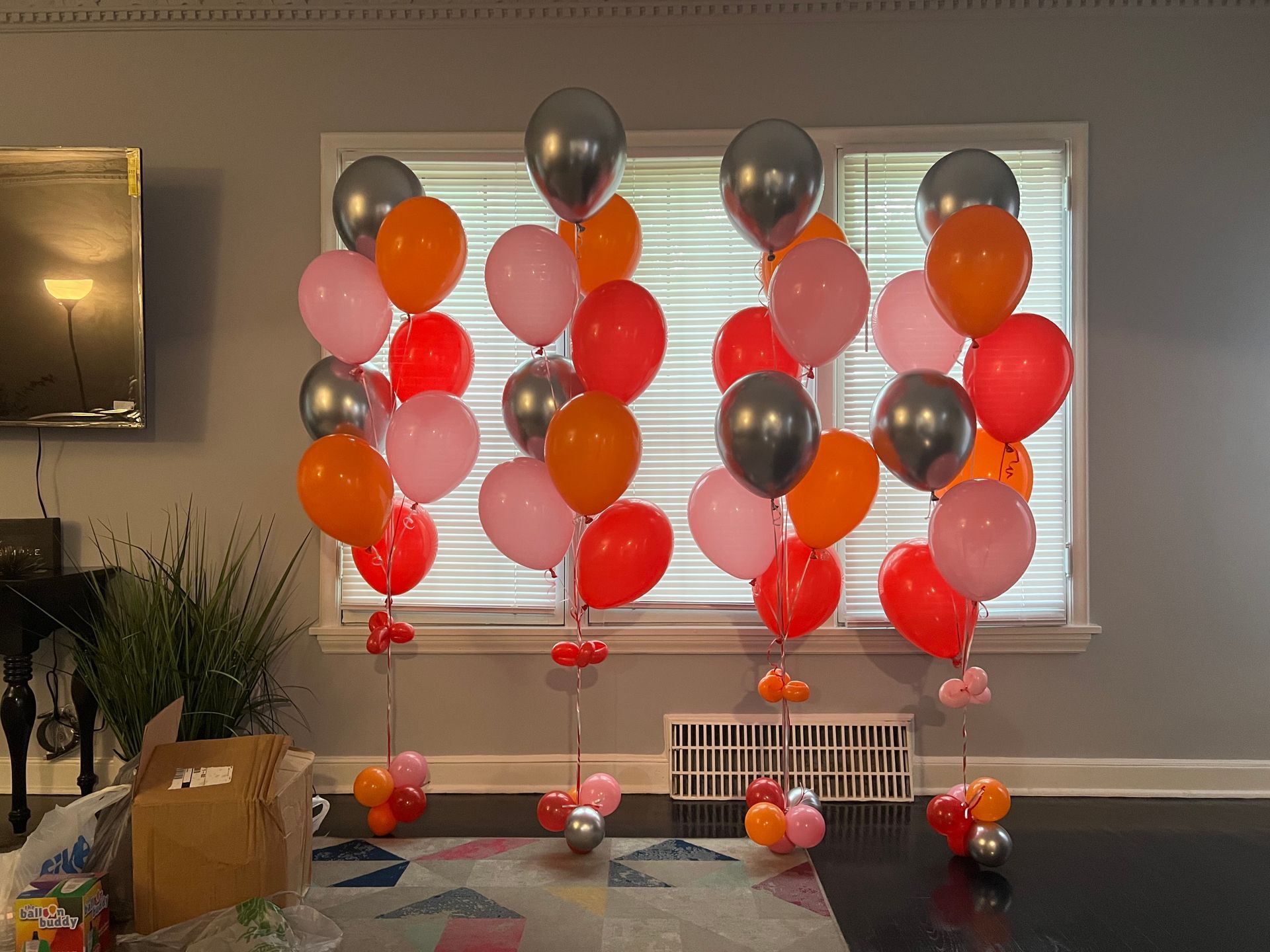 A bunch of balloons are sitting in front of a window in a living room.