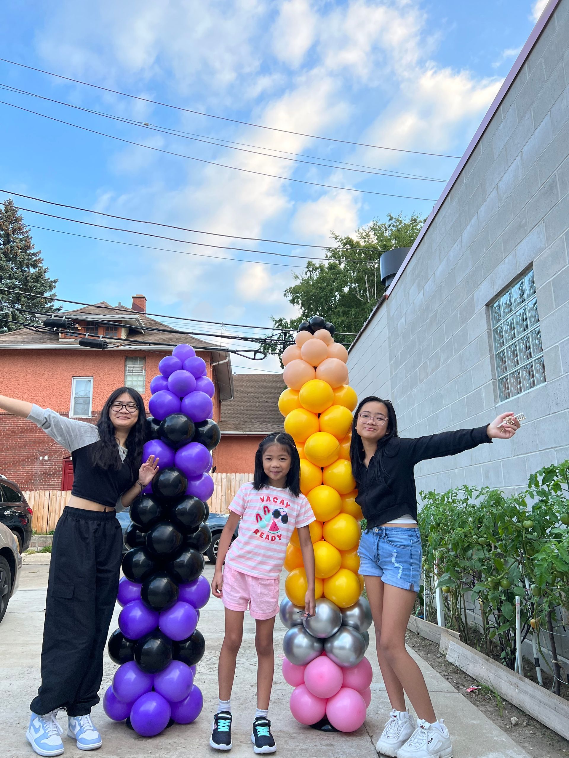 Three girls are standing next to each other in front of a row of balloons.