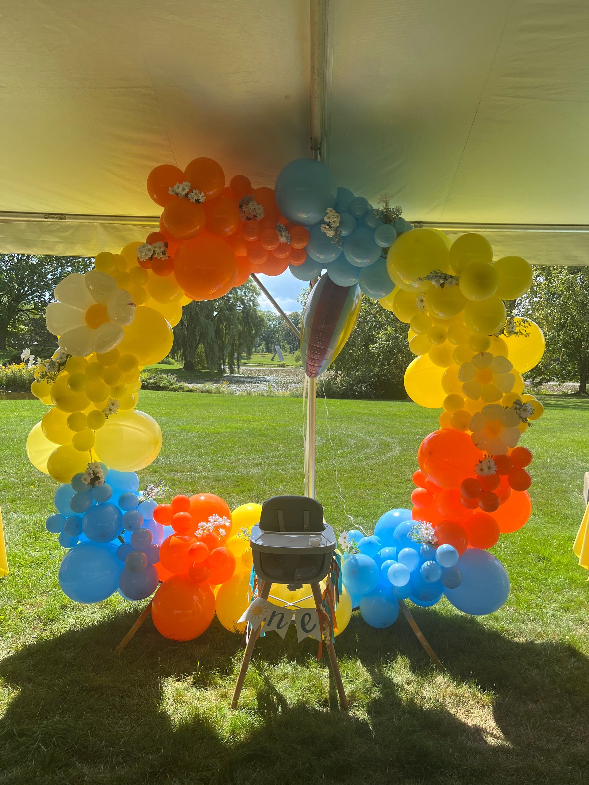 A baby chair is under a tent decorated with balloons.