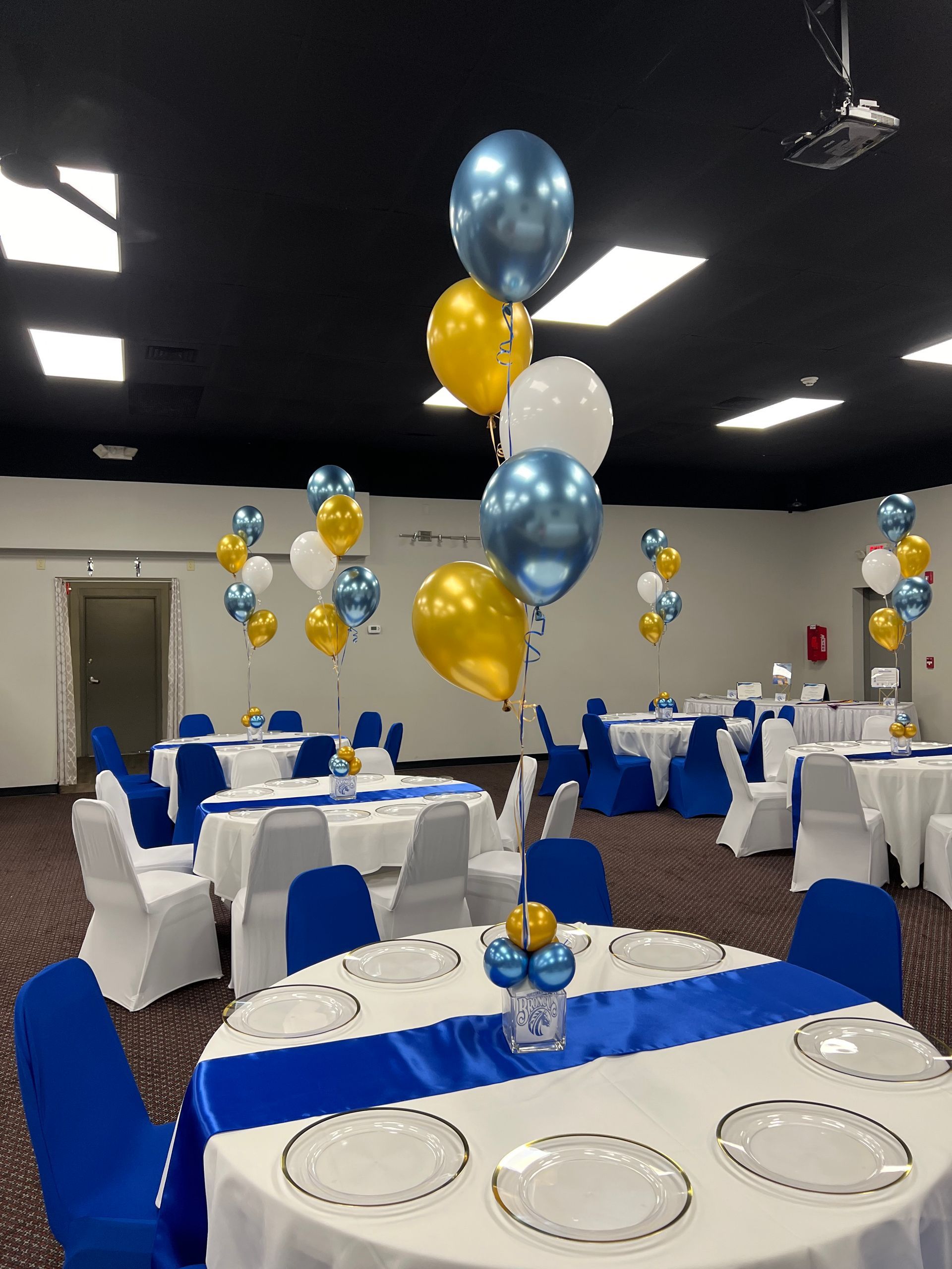 A large room with tables and chairs decorated with blue and gold balloons