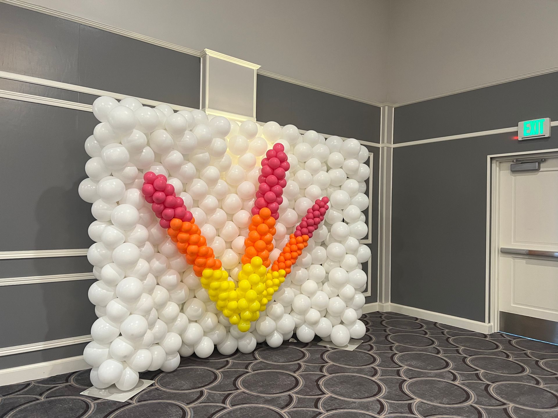 A wall made of balloons in a room with a logo on it.