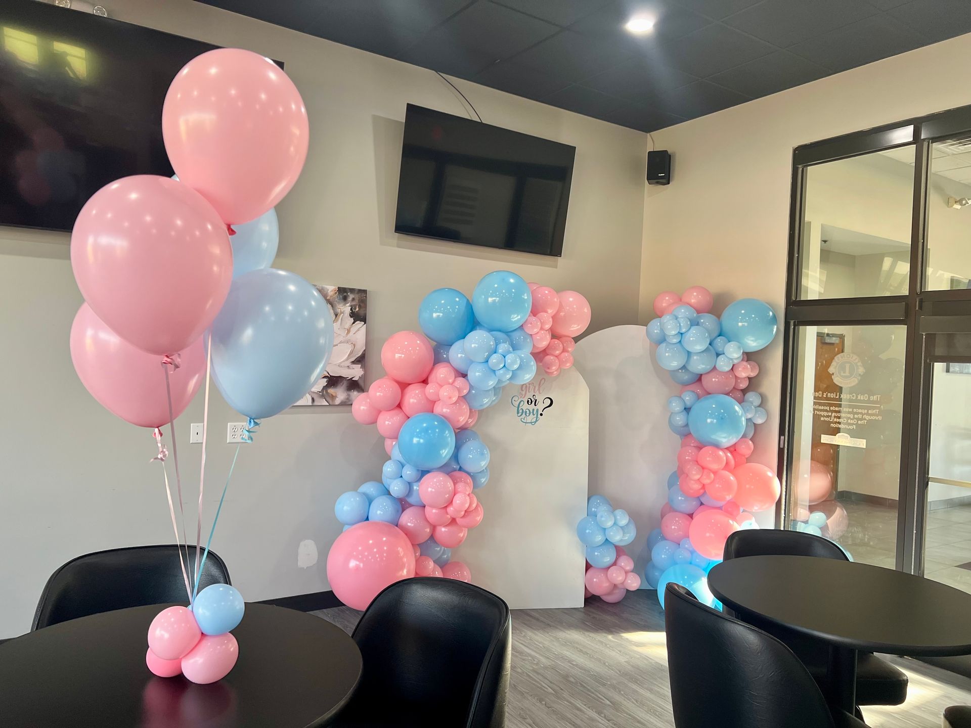 A room with tables and chairs decorated with pink and blue balloons.