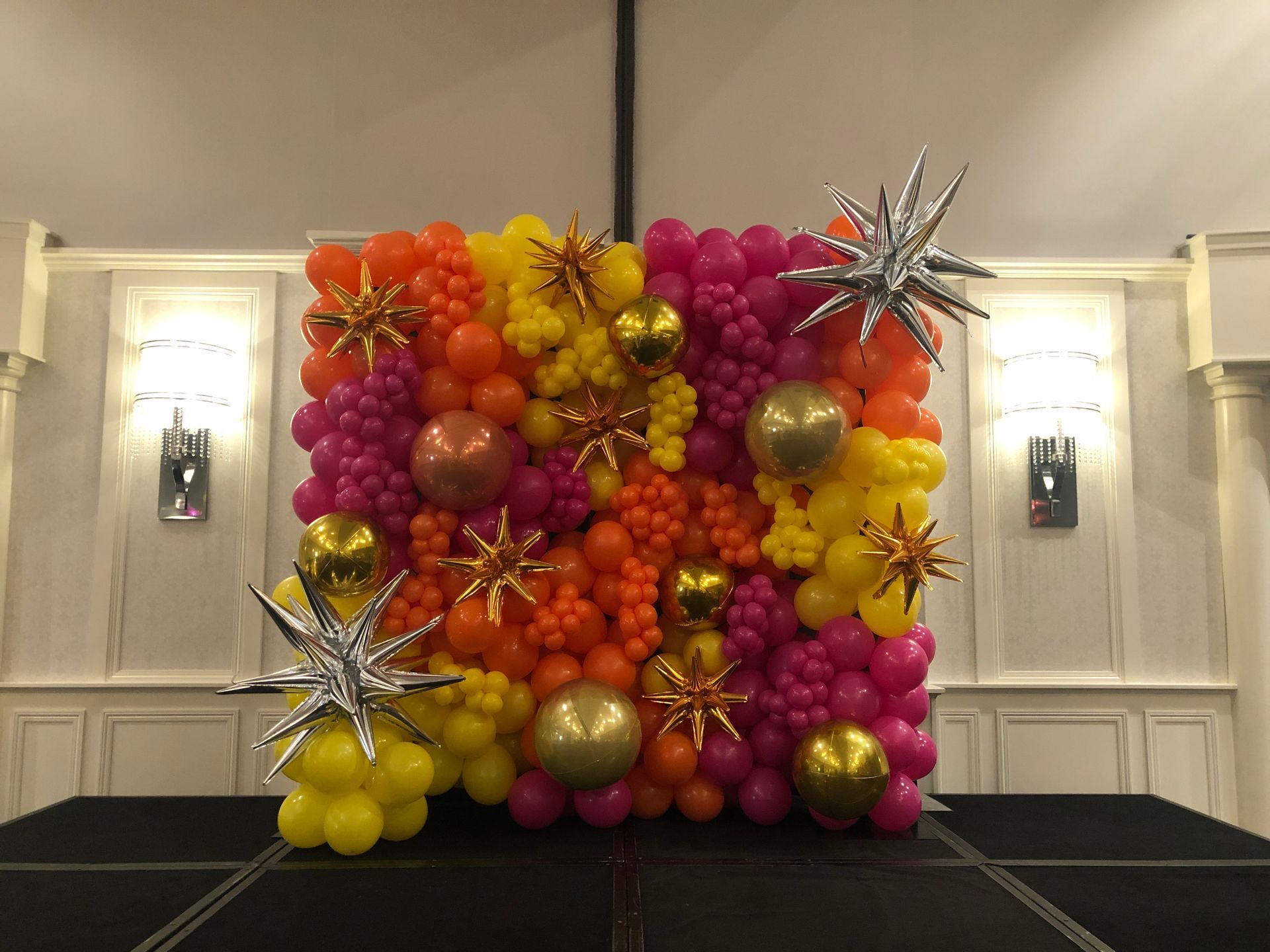A colorful balloon wall is sitting on top of a stage in a room.