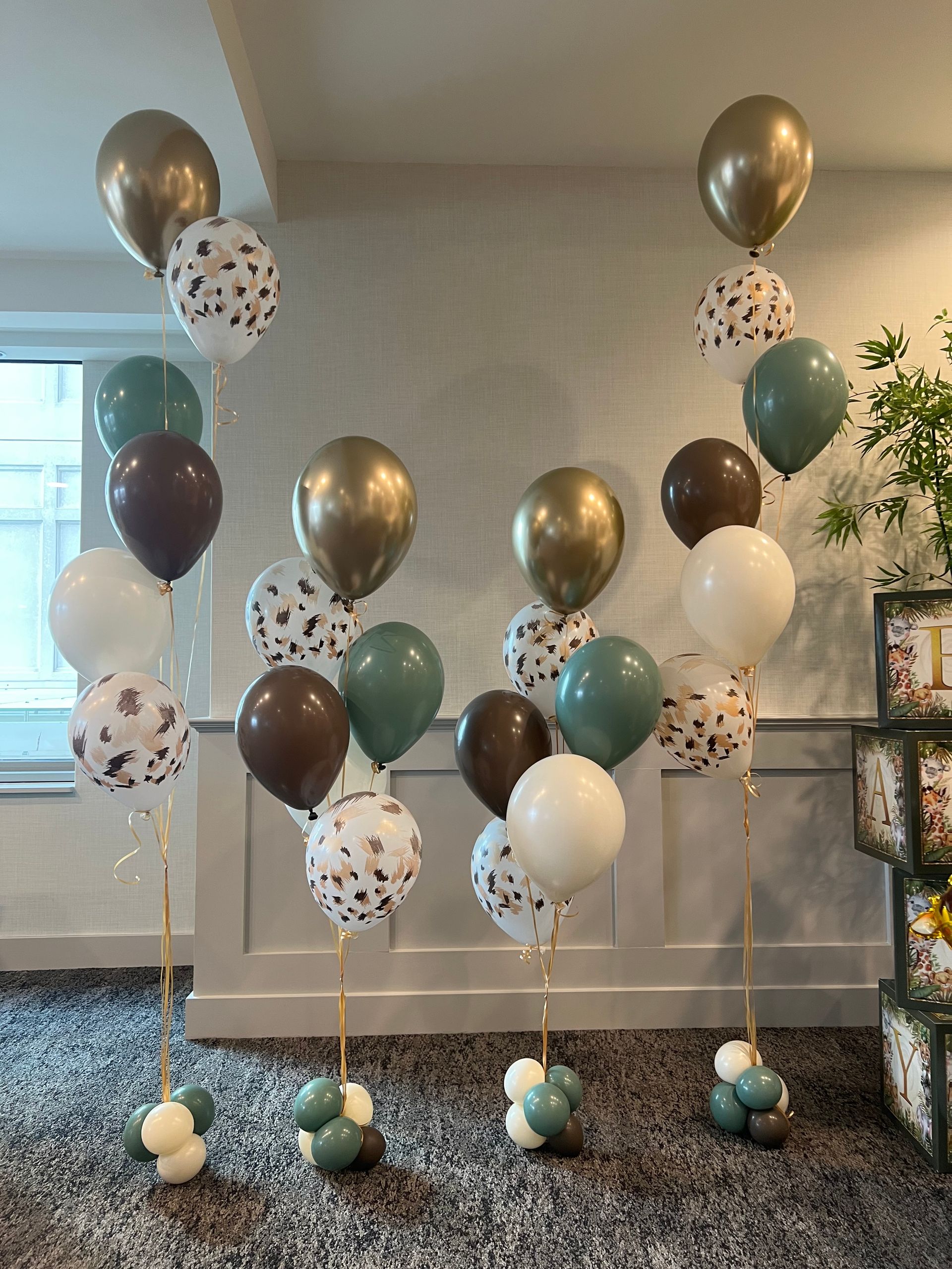 Balloon display with gold, white, brown, teal, and confetti balloons in a living room.