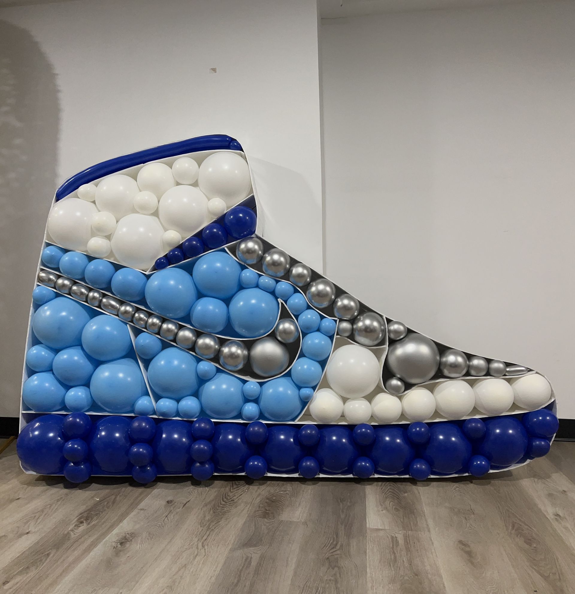 A shoe made of balloons is sitting on a wooden floor.