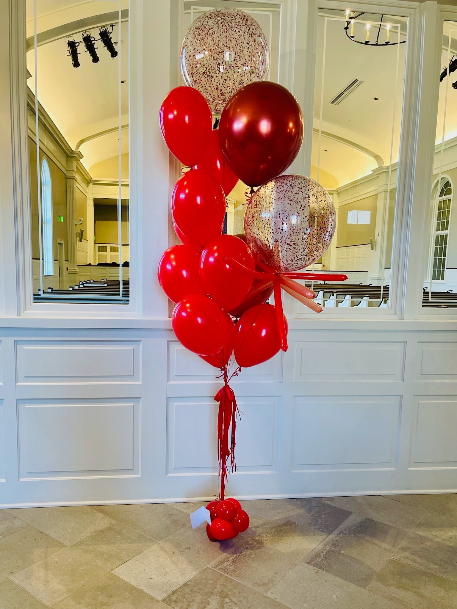 A bunch of red balloons are sitting in front of a white wall.