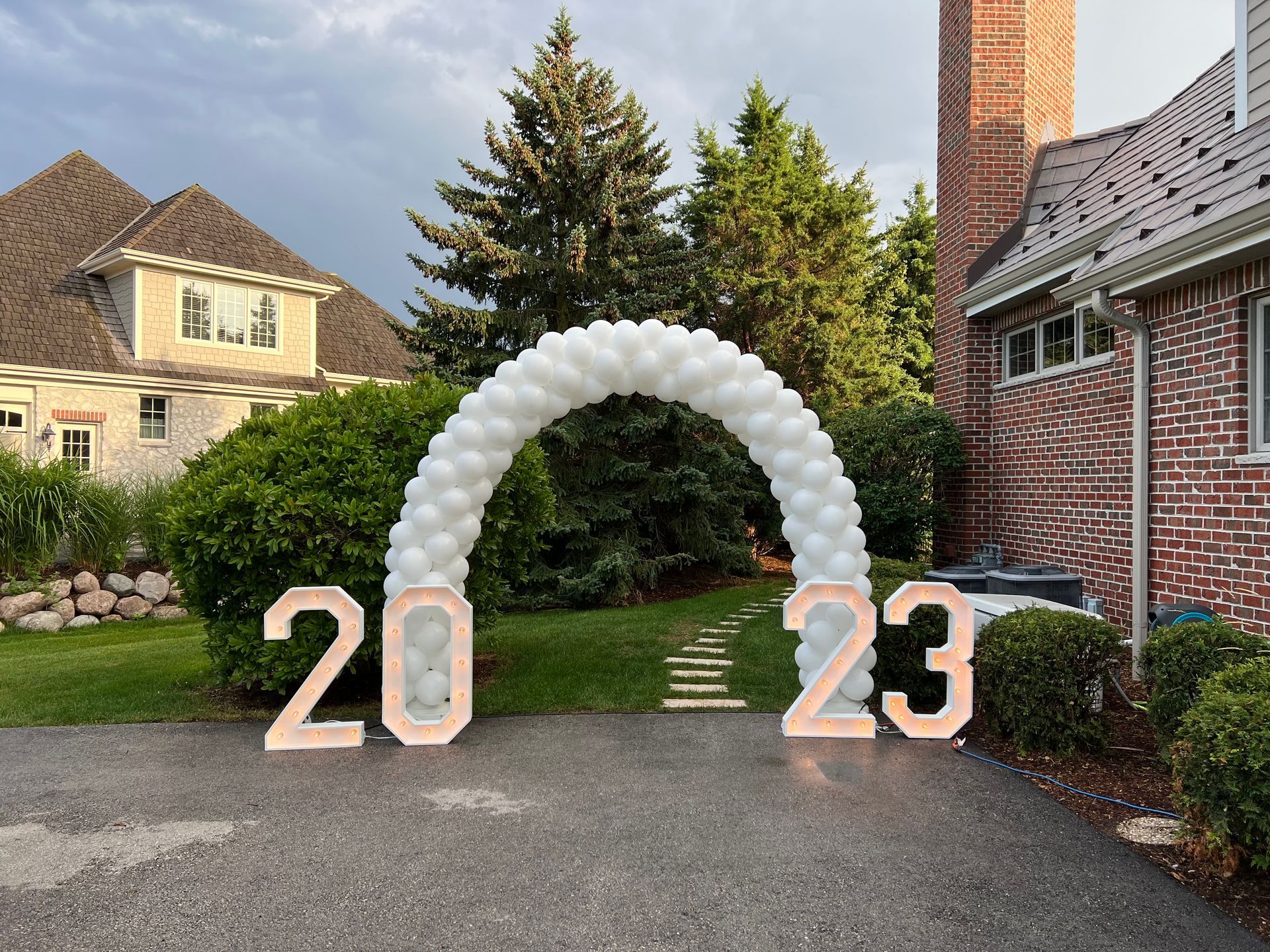 A white balloon arch with the numbers 20 and 23 in front of a brick house.