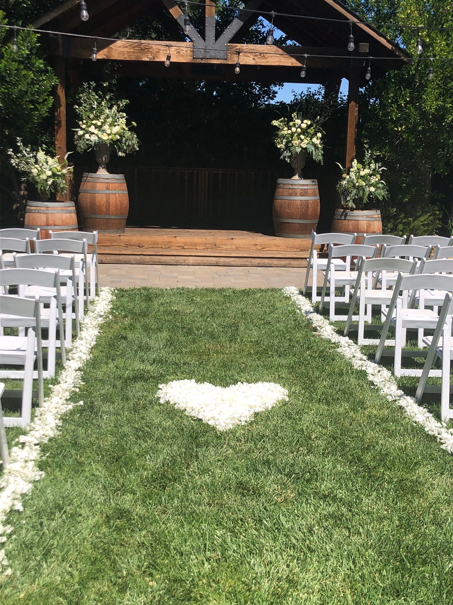 A wedding ceremony is taking place in front of a gazebo with a heart of petals made of carnation confetti in the grass.