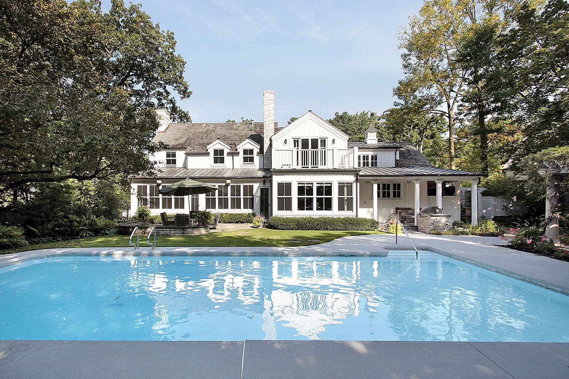 A large, two-story white house with a swimming pool in the foreground, surrounded by mature trees.