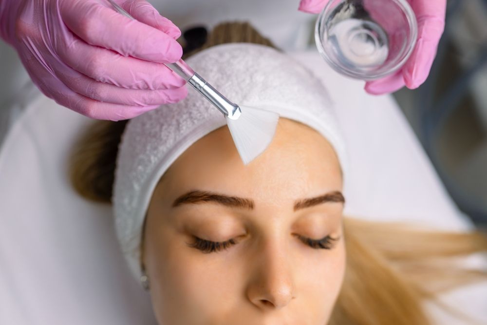 Aesthetic treatment applied to a woman’s forehead with a brush and cotton pad, wearing a headband.