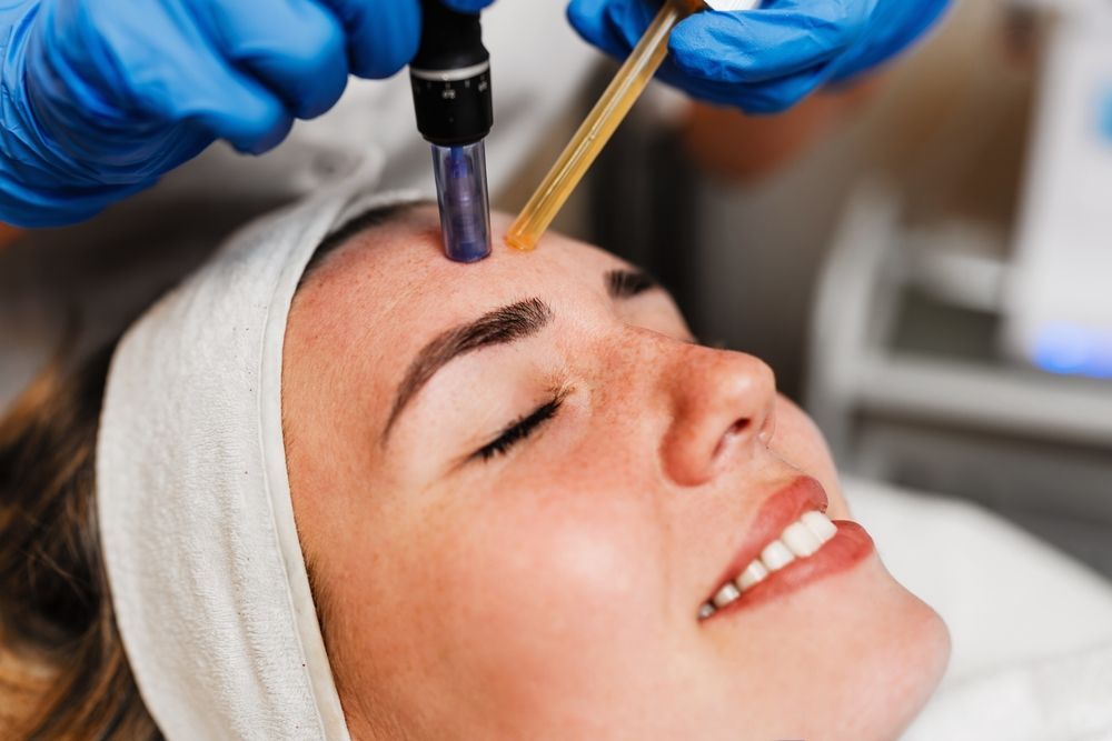 Cosmetic treatment applying serum to a woman’s forehead with a dropper and brush