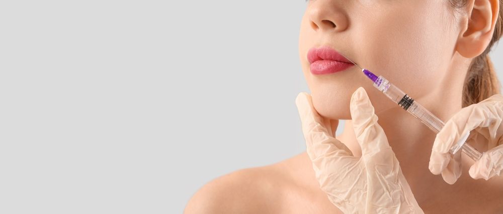 Gloved hands inject filler into a woman’s lips with a syringe