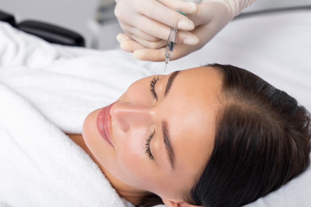 Beauty technician applying eyebrow treatment with a handheld tool to a client lying on a bed