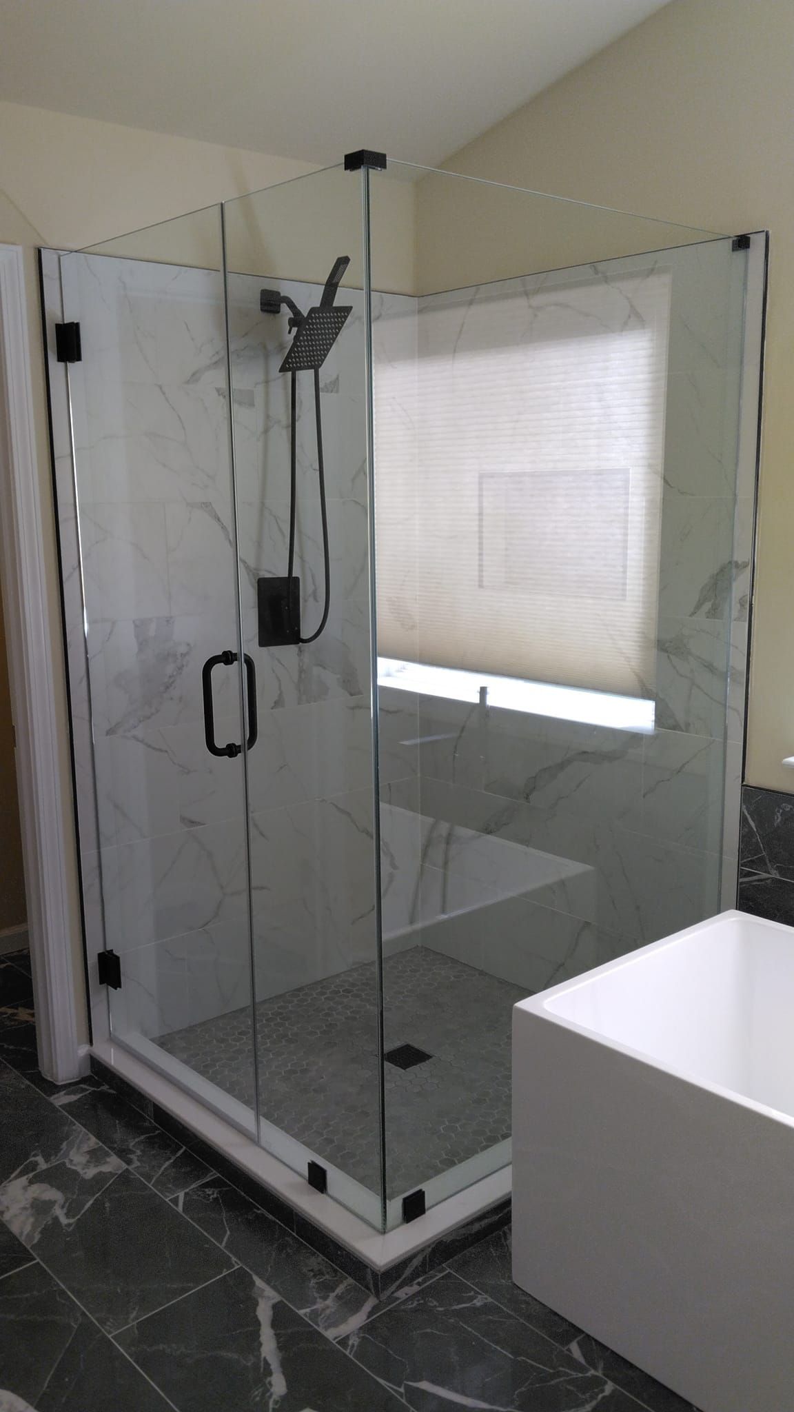 Corner glass shower enclosure with marble-look tile, black fixtures, and a white, contemporary-style tub.