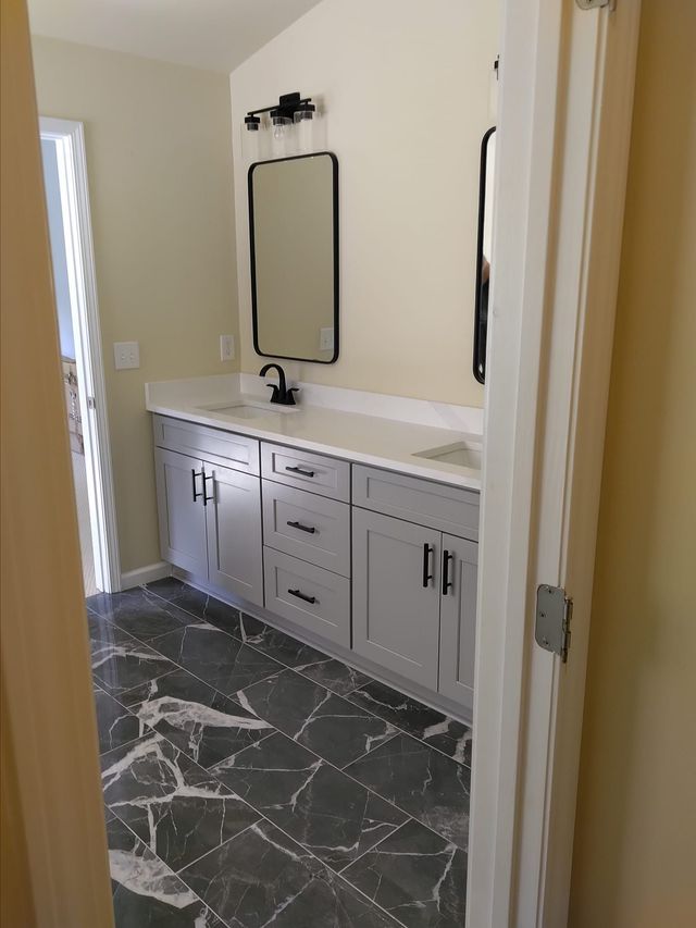 Bathroom with gray vanity, black fixtures, marble-look floor, and a mirror.