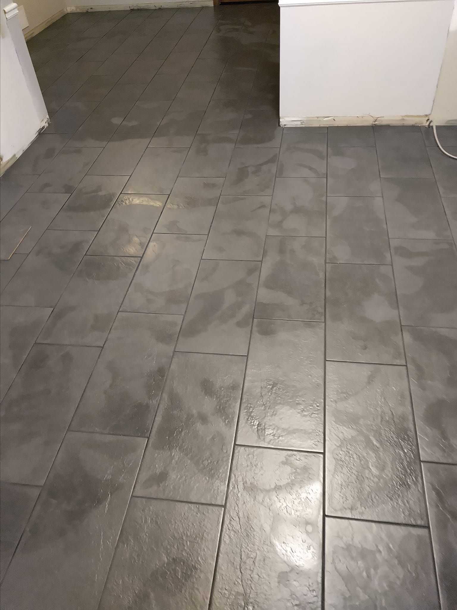 Gray tiled floor with rectangular tiles in a room with white walls.