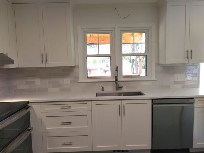 White kitchen cabinets with a window above a sink and a stainless steel dishwasher.