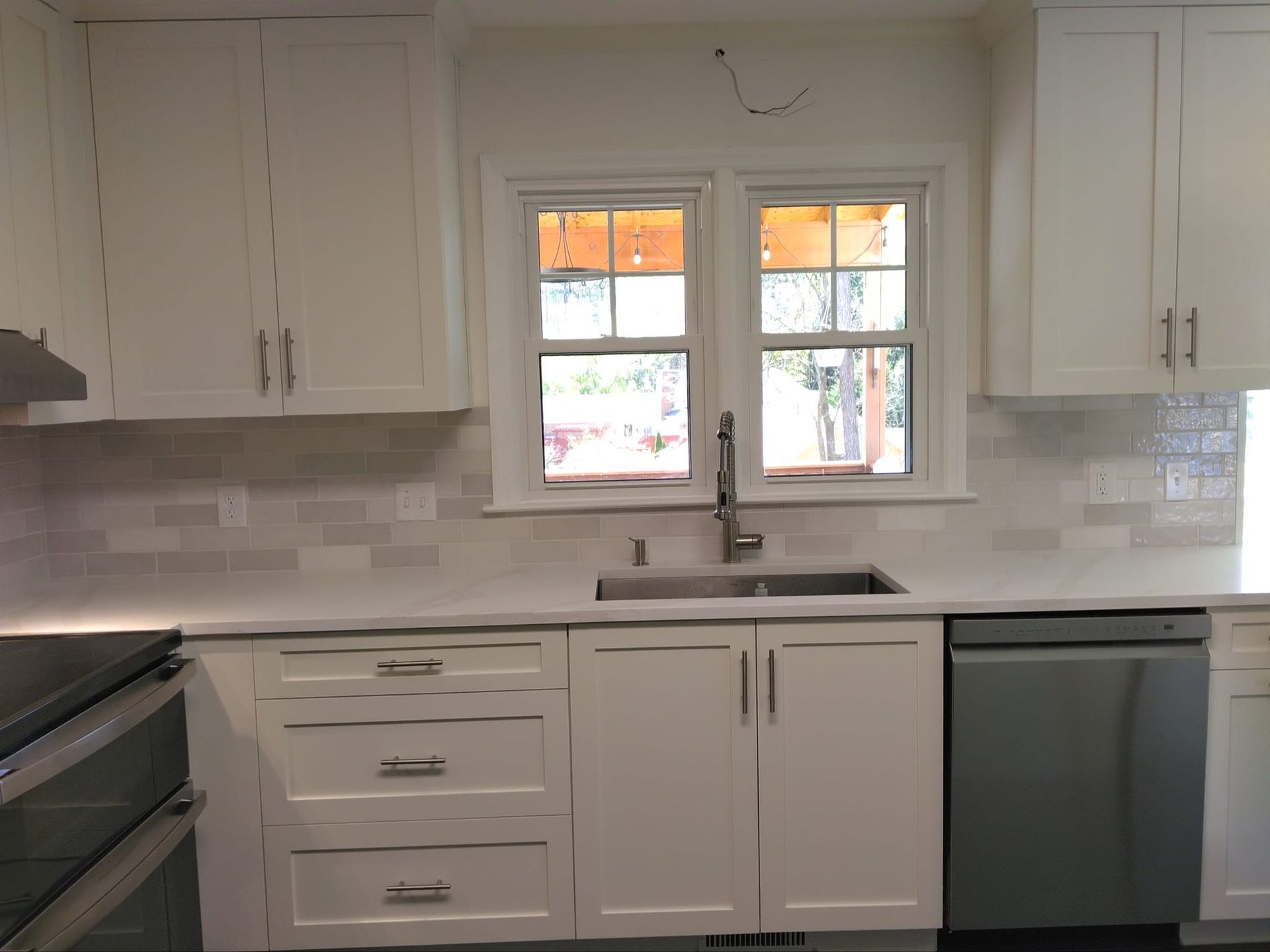 White kitchen with cabinets, window over sink, and stainless steel appliances.