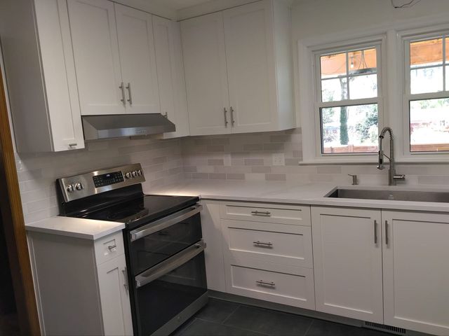 White kitchen cabinets with stainless steel oven, backsplash, and sink.