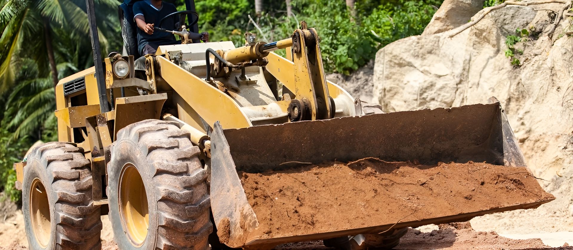 A Man Is Driving A Bulldozer On A Dirt Road — Arnway Pty Ltd In South West Rocks, NSW