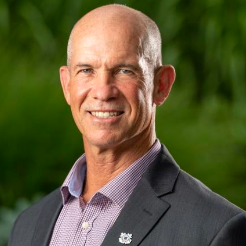 A bald man in a suit and purple shirt is smiling for the camera.