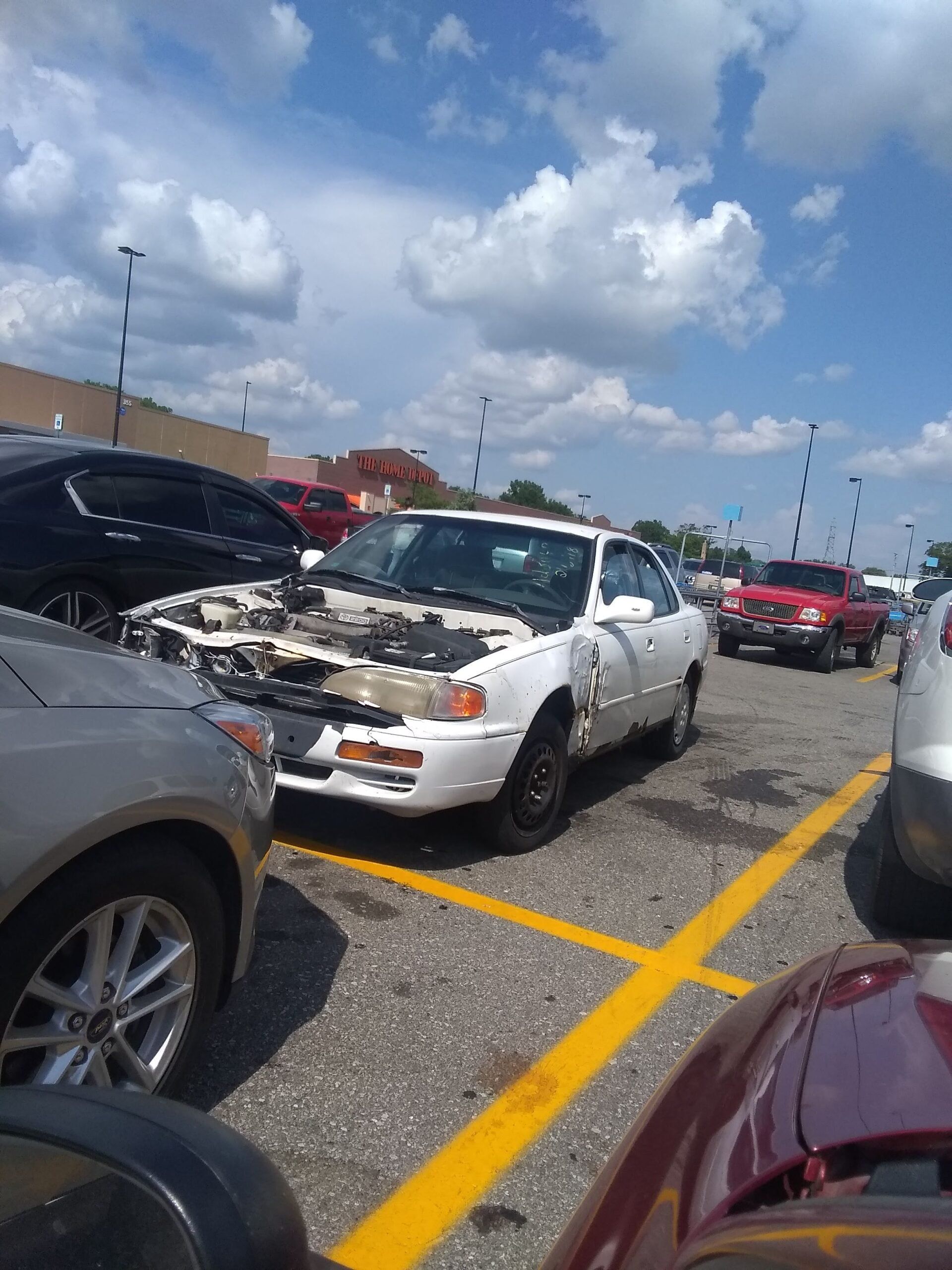 A white car with its hood up is parked in a parking lot