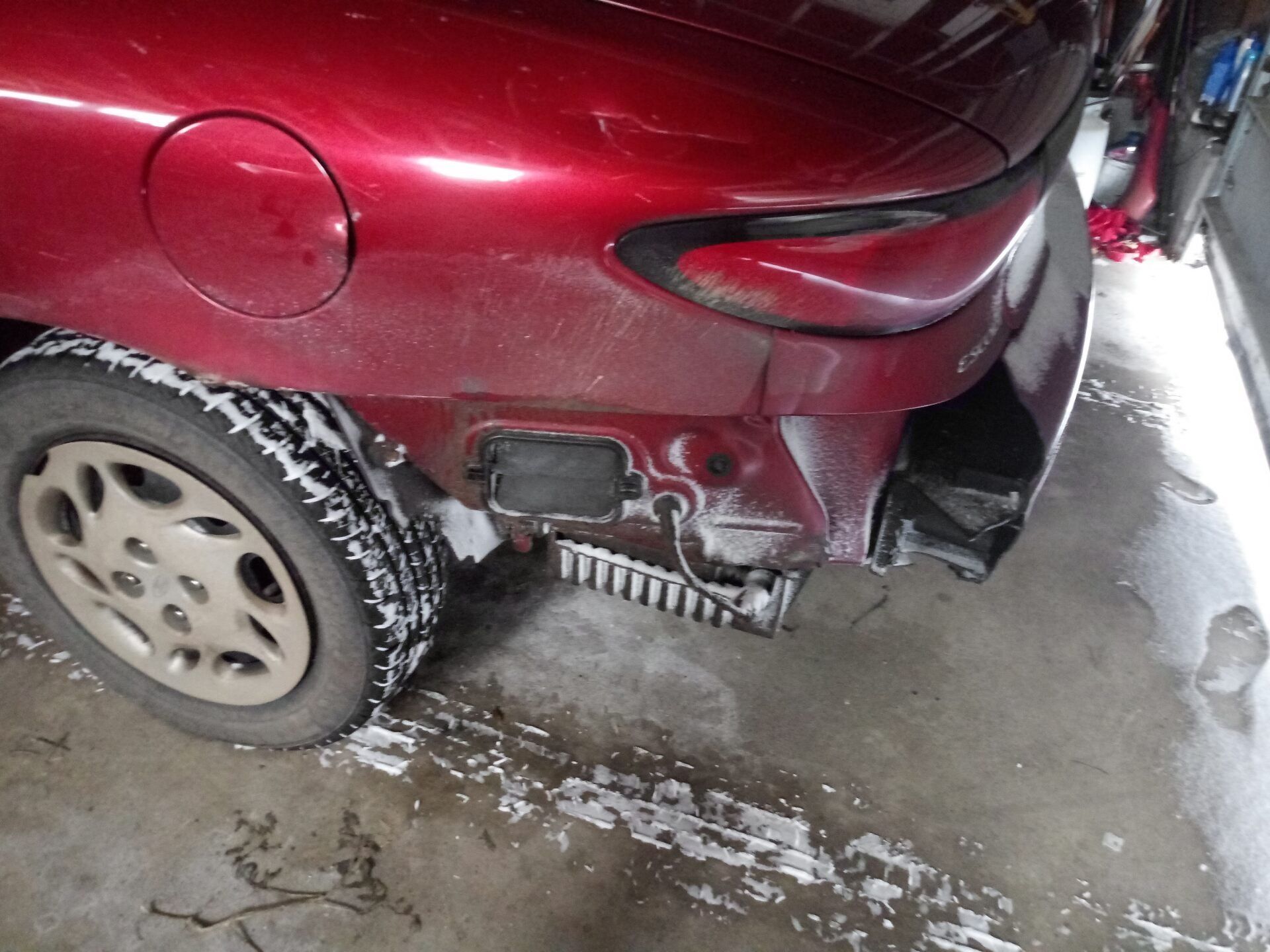 A red car is sitting in a garage with the bumper removed