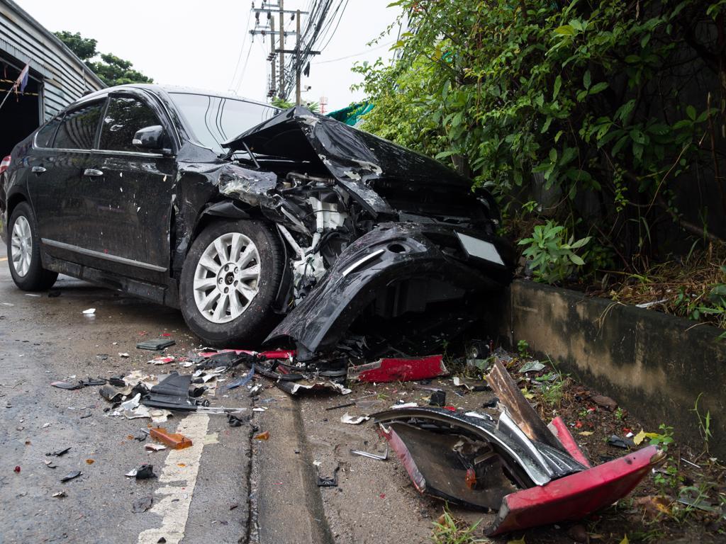 A black car has been damaged in a car accident on the side of the road.