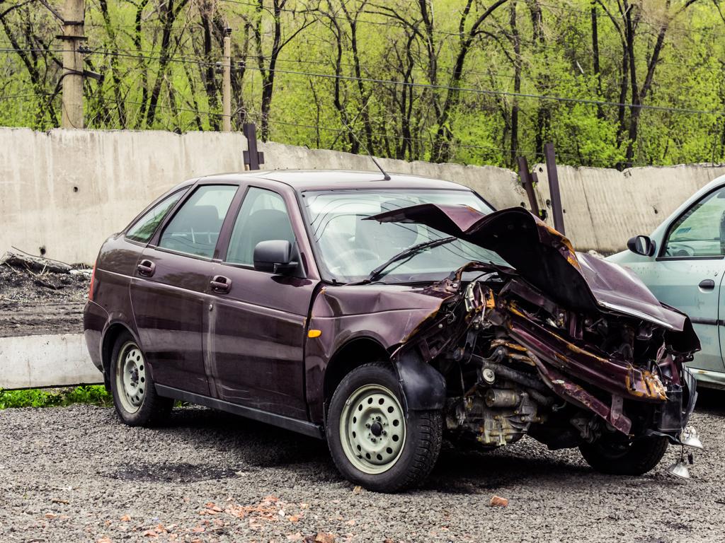 A wrecked car is parked in a gravel lot.