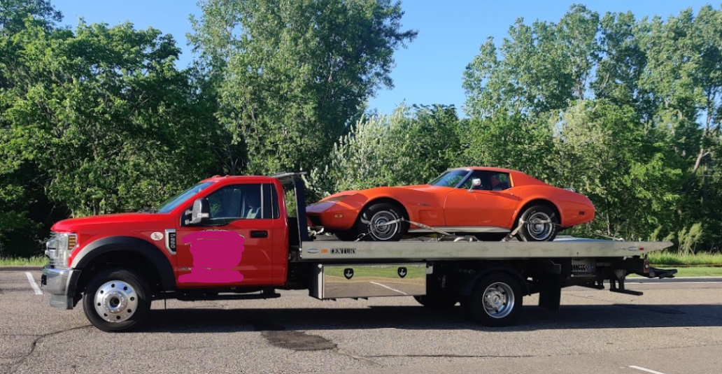 A red tow truck is carrying an orange corvette