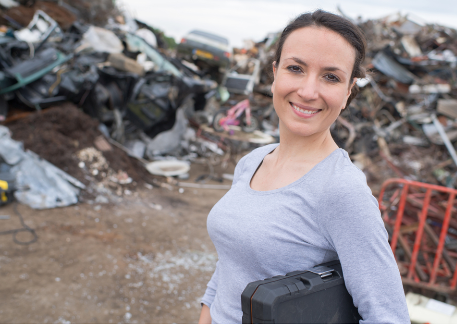 A woman is standing in front of a pile of scrap metal
