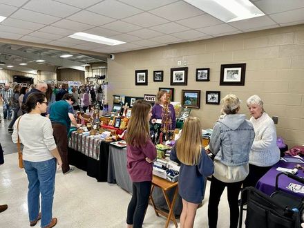 Art fair: people browse booths inside and outside a building. Artwork, decor, and tents are visible.
