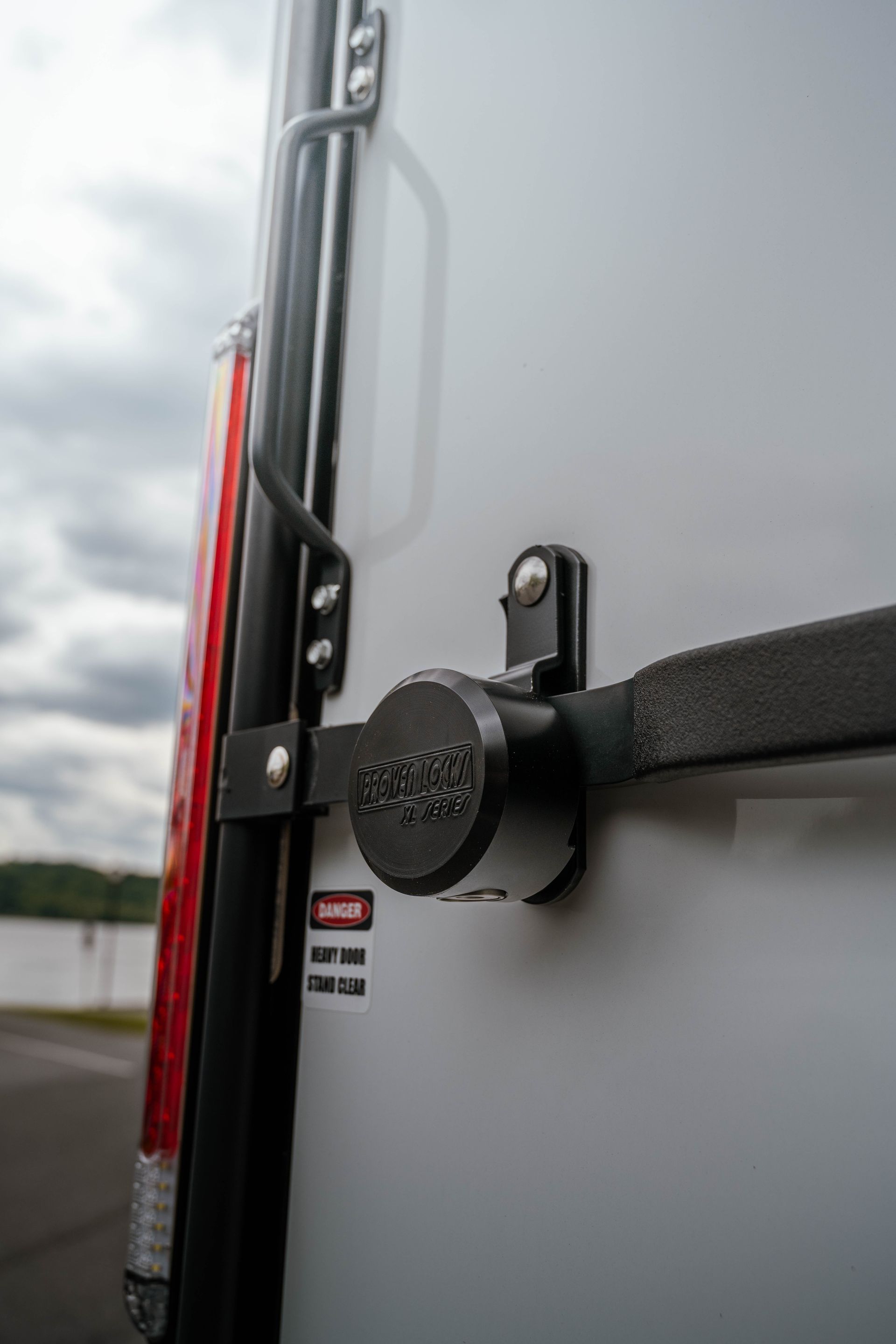 Black lock mechanism on a white van door, near a red taillight and warning label.