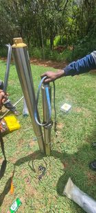 A person holding a submersible pump with a green grassy backdrop and a tree line in the background.