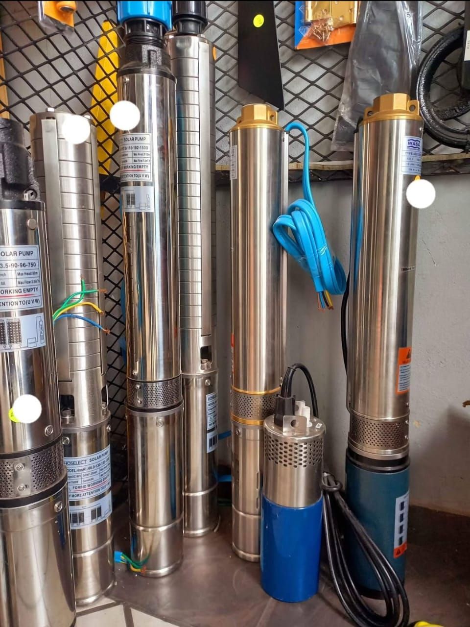 Several cylindrical submersible water pumps with various colored cords and components on a metal surface.