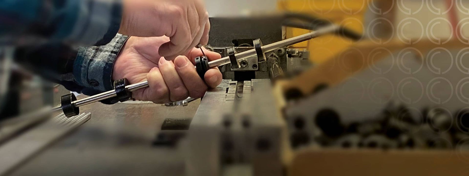 Person's hands working on a metal machine, holding a tool, focused on the task in a workshop.