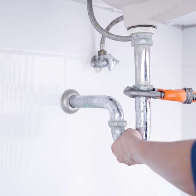 a person is fixing a sink pipe with a wrench .