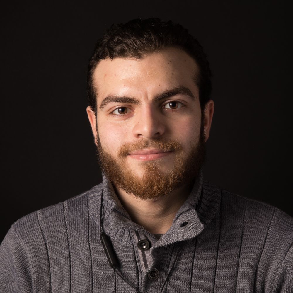 a man with a beard is wearing a grey sweater and smiling for the camera .