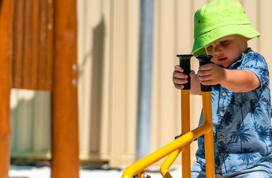 Baby in green hat playing outside on yellow play equipment