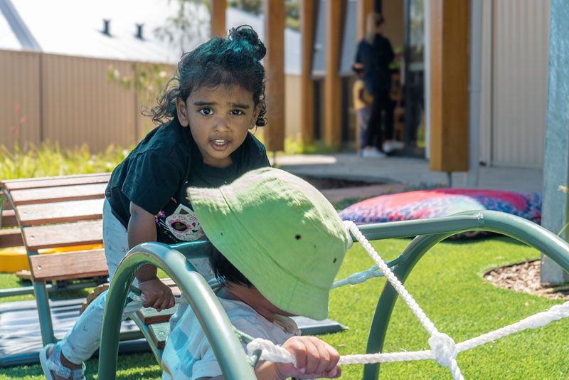 Toddler Playing Outside on Play equipment | Toddler facing camera | Second toddler in foreground wearing oversize green hat