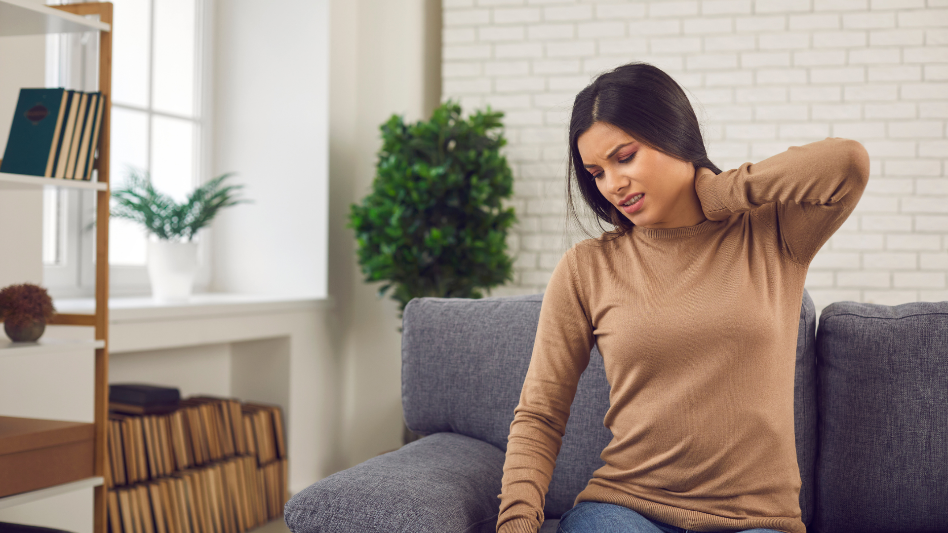 a woman is sitting on a couch with a sore neck .