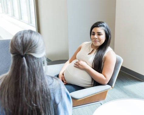 A smiling expectant mother holding her belly while sitting with a counselor.