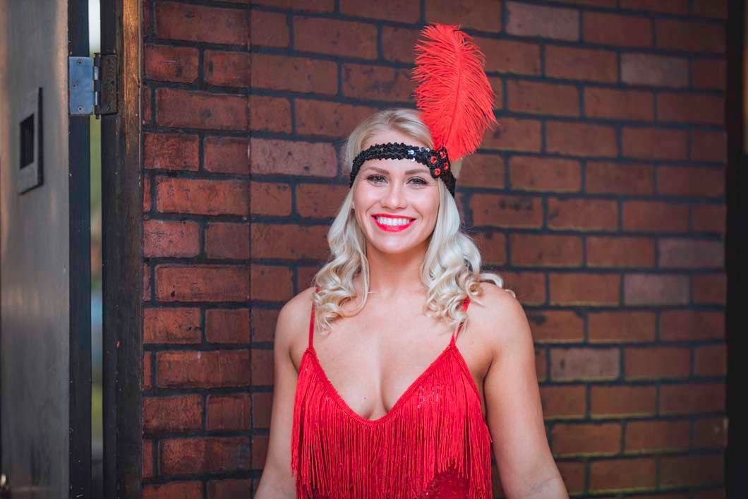 A woman in a red dress and headband is standing in front of a brick wall.