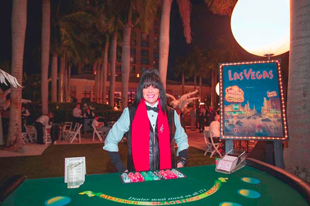 A woman in a red scarf is standing in front of a poker table.