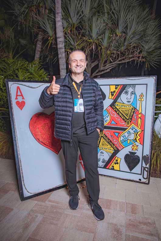 A man is standing in front of a large playing card and giving a thumbs up.