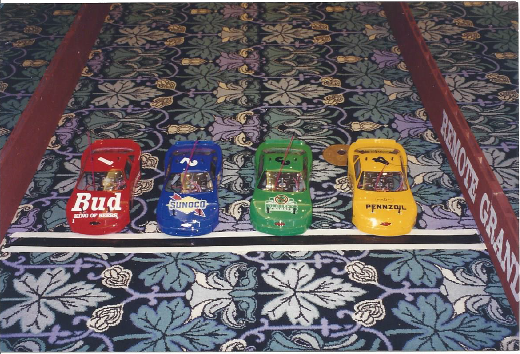 Four toy cars are lined up on a carpet and one of them has the word bud on it