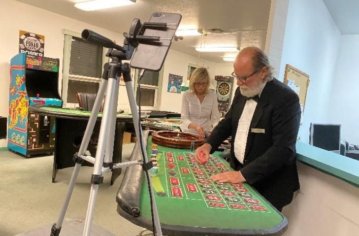 A man in a tuxedo is playing roulette in a casino while a woman watches.