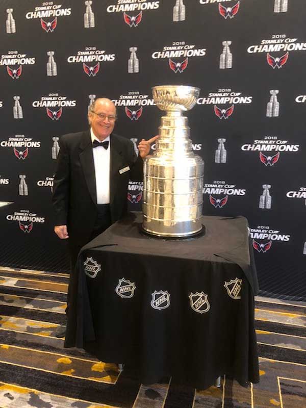 A man in a tuxedo is standing next to a trophy.