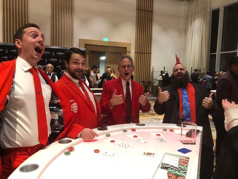 A group of men in red suits and ties are standing around a table.